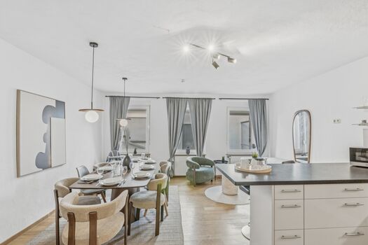 Langer heller Esstisch mit beigen Stühlen, von Hängeleuchten beleuchtet, große Fenster mit Vorhängen Langer heller Esstisch mit beigen Stühlen, von Hängeleuchten beleuchtet, große Fenster mit Vorhängen