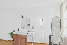 Weißer Schminktisch mit zwei ovalen Spiegeln, terrakottafarbener Sessel, großer Standspiegel, Zimmerpflanze. Weißer Schminktisch mit zwei ovalen Spiegeln, terrakottafarbener Sessel, großer Standspiegel, Zimmerpflanze.