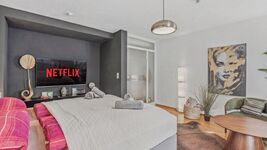 Großes Doppelbett mit grauer Bettwäsche, Fernseher mit Netflix-Logo an der dunklen Wand. Großes Doppelbett mit grauer Bettwäsche, Fernseher mit Netflix-Logo an der dunklen Wand.
