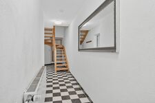 Flur mit schwarz-weißem Schachbrettmuster, Holztreppe, großer Wandspiegel, hohe Decken. Flur mit schwarz-weißem Schachbrettmuster, Holztreppe, großer Wandspiegel, hohe Decken.