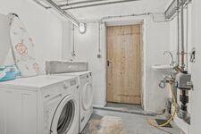 Weiße Einbauwaschmaschine in einem schlichten Hauswirtschaftsraum mit Holztür. Weiße Einbauwaschmaschine in einem schlichten Hauswirtschaftsraum mit Holztür.