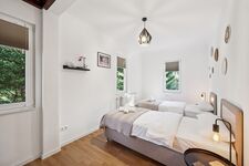 Schlafzimmer 1 mit hochwertigen Boxspringbetten, Nachttischen und einem offenen Kleiderschrank sowie Blick ins Grüne. Die Betten können wahlweise einzeln oder als komfortables Doppelbett gestellt werden. Schlafzimmer 1 mit hochwertigen Boxspringbetten, Nachttischen und einem offenen Kleiderschrank sowie Blick ins Grüne. Die Betten können wahlweise einzeln oder als komfortables Doppelbett gestellt werden.