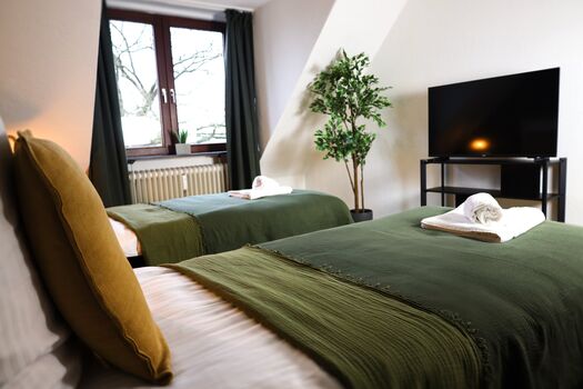 Schlafzimmer 1 - Twin-Schlafzimmer mit zwei Einzelbetten, hochwertiger Bettwäsche, TV, Nachttischlampen und ruhigen Grüntönen. Schlafzimmer 1 - Twin-Schlafzimmer mit zwei Einzelbetten, hochwertiger Bettwäsche, TV, Nachttischlampen und ruhigen Grüntönen.