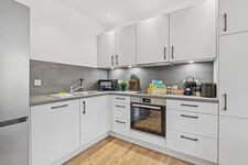 Weiße L-Küche mit grauer Arbeitsplatte, Backofen, Mikrowelle, Fenster mit Grünblick. Weiße L-Küche mit grauer Arbeitsplatte, Backofen, Mikrowelle, Fenster mit Grünblick.