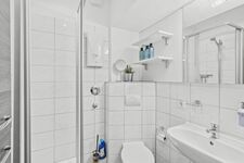 Weiß gefliestes Badezimmer mit Glasdusche, WC, Wandregal mit Pflegeprodukten. Weiß gefliestes Badezimmer mit Glasdusche, WC, Wandregal mit Pflegeprodukten.