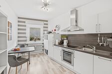 Weiße L-Küche mit grauer Arbeitsplatte, Dunstabzugshaube, Backofen und hellem Holzparkett. Weiße L-Küche mit grauer Arbeitsplatte, Dunstabzugshaube, Backofen und hellem Holzparkett.