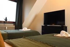 Schlafzimmer 1 - Twin-Schlafzimmer mit zwei Einzelbetten, hochwertiger Bettwäsche, TV, Nachttischlampen und ruhigen Grüntönen.