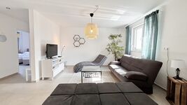 Modernes Wohnzimmer mit gemütlicher Sitzecke, Flachbild-TV, stilvoller Beleuchtung, hellen Fliesen, großen Fenstern und geschmackvoller Deko.