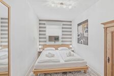 Doppelbett mit weißer Bettwäsche auf Holzrahmen, grau-weiß gestreifte Wandtapete